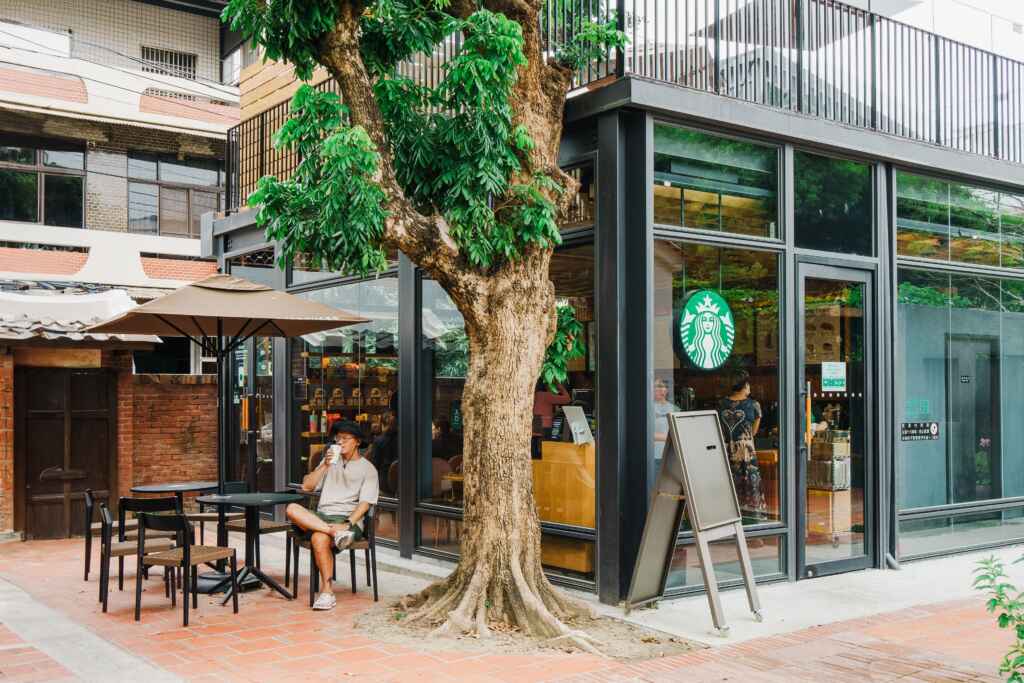 ▲來新港，遊客可以坐在龍眼樹下喝星巴克咖啡。（嘉義縣政府提供）